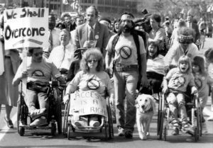 A black and white picture of disability advocates making a protest march in the 1970s.