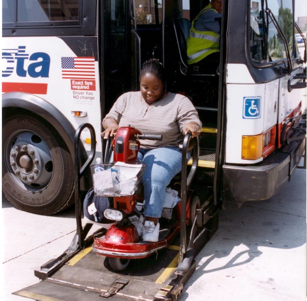 A woman using an electric scooter rides a lift to get onto a bus.