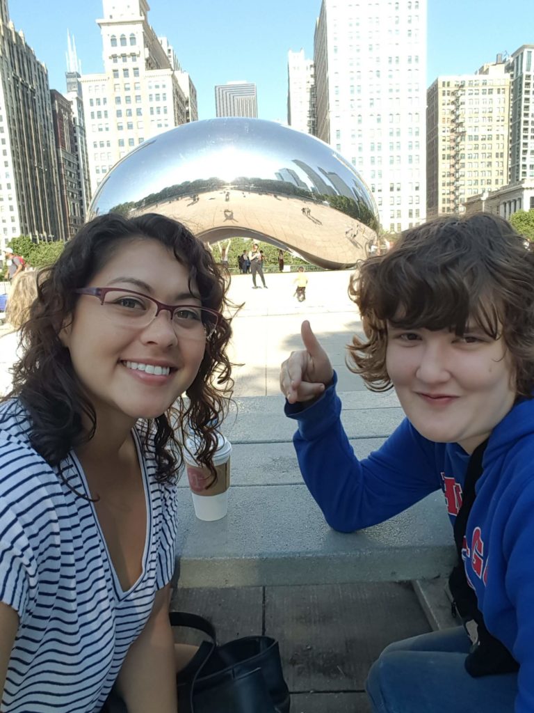 A young woman and a teenage girl posing for a picture together in front of "The Bean".