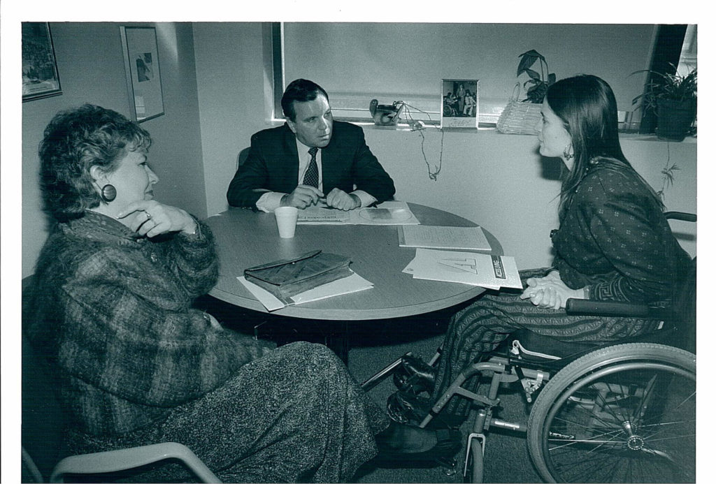 A black and white photo of disability rights activist Marca Bristo in a meeting with Mayor Richard Daley and Maggie Daley.