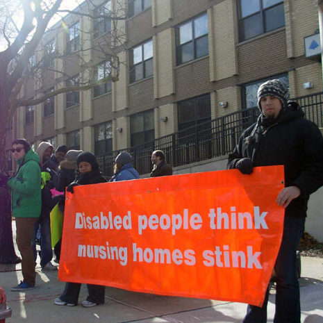 Protestors carrying a sign that reads, "Disabled people think nursing homes stink."