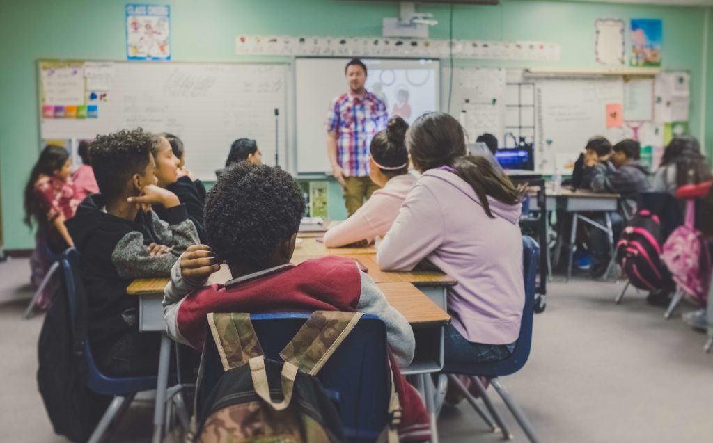 Kids in a classroom, listening to their teacher.