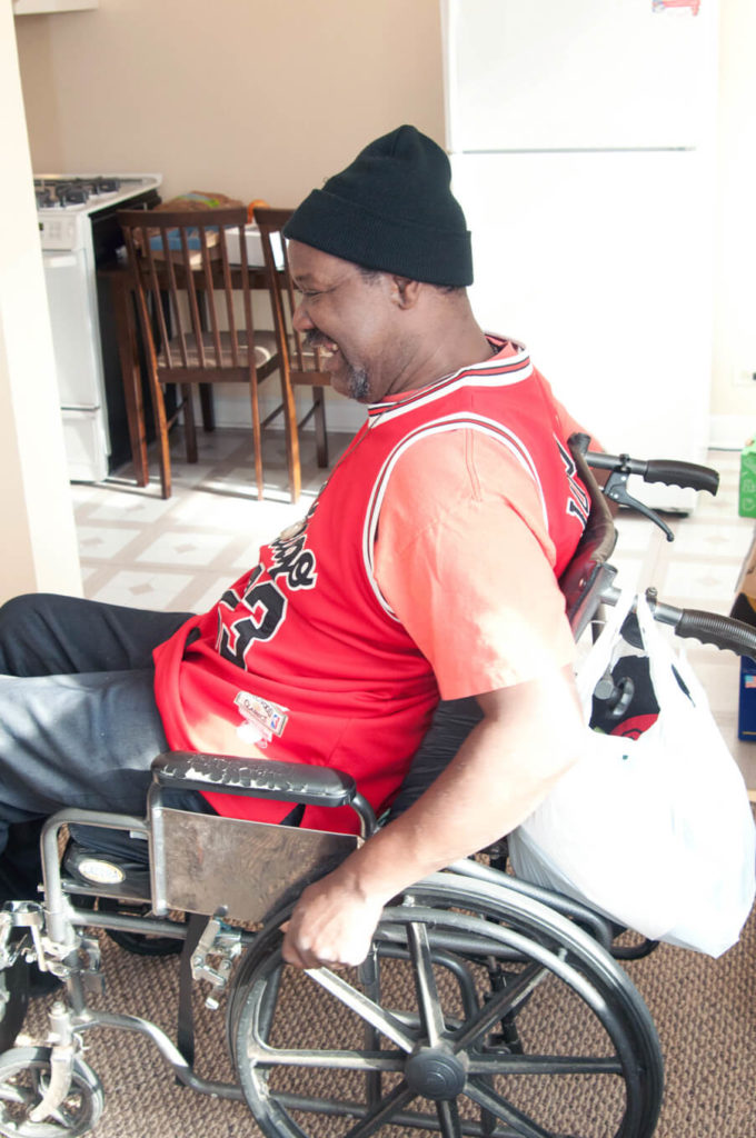 A Black man, a wheelchair user, smiles as he moves into his own home.