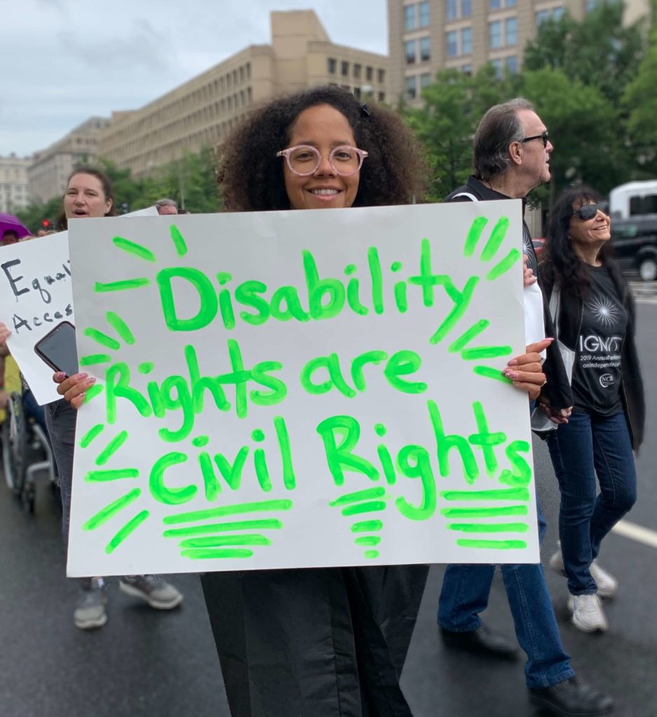 A young Black woman carrying a sign that reads, 'Disability rights are civil rights'.