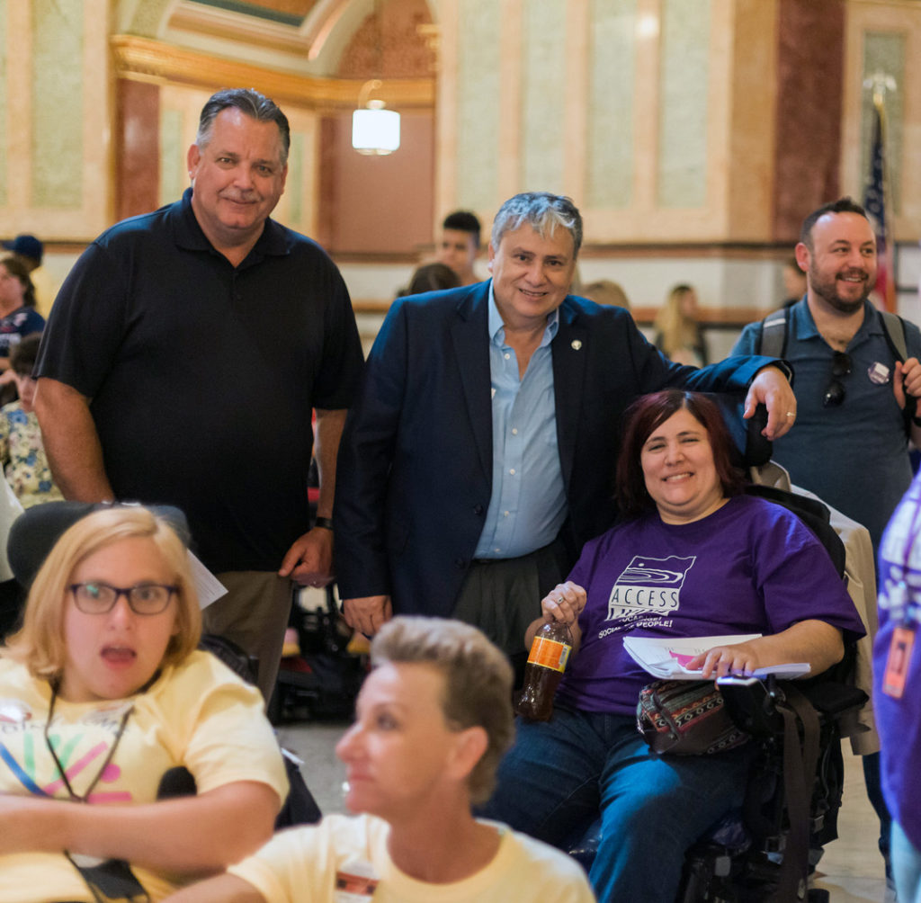 Immigration advocates, two are men who are standing and a woman using a wheelchair attending a rally.