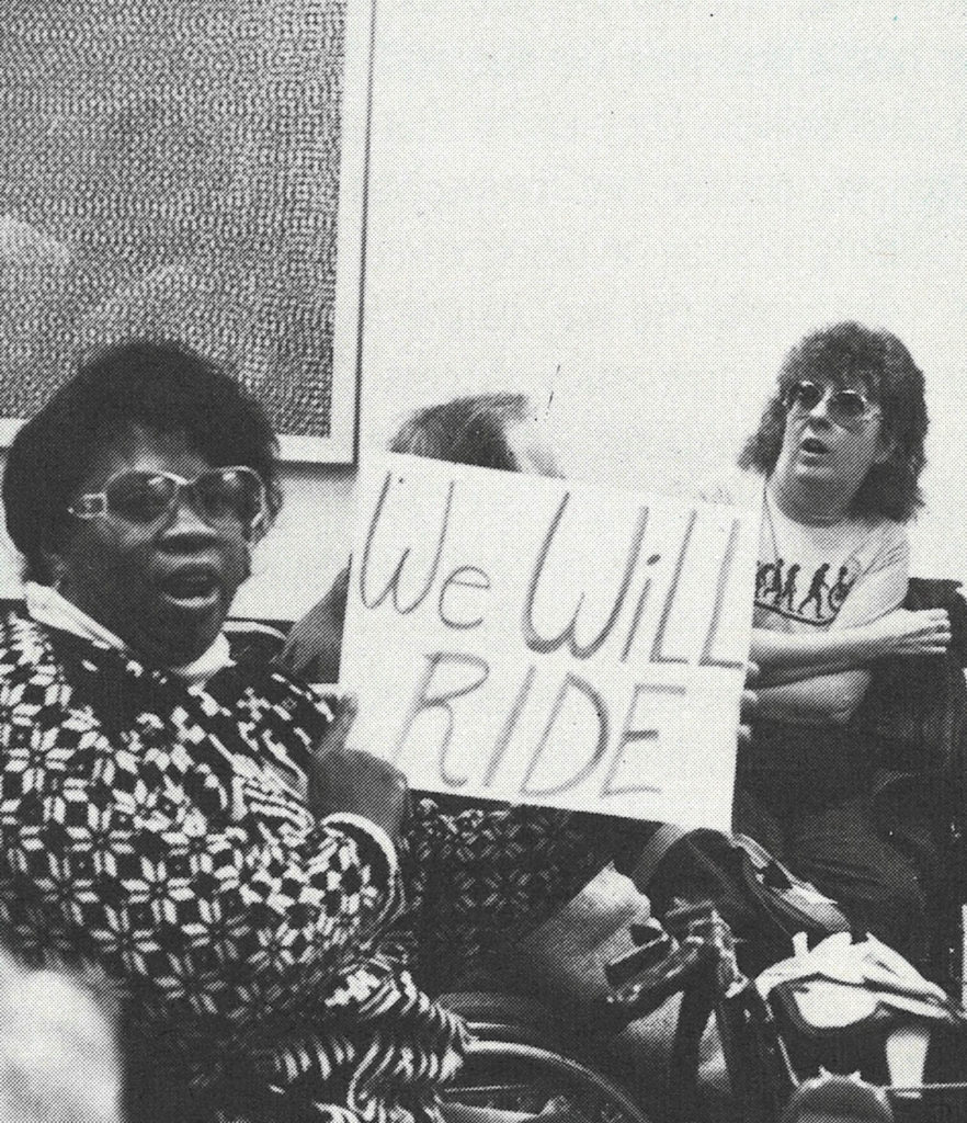 A Black woman holding a protest sign that says, "We Will Ride."