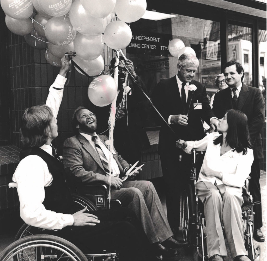 Three wheelchair users, including Marca Bristo, cut celebratory balloons in front of Access Living's original location.