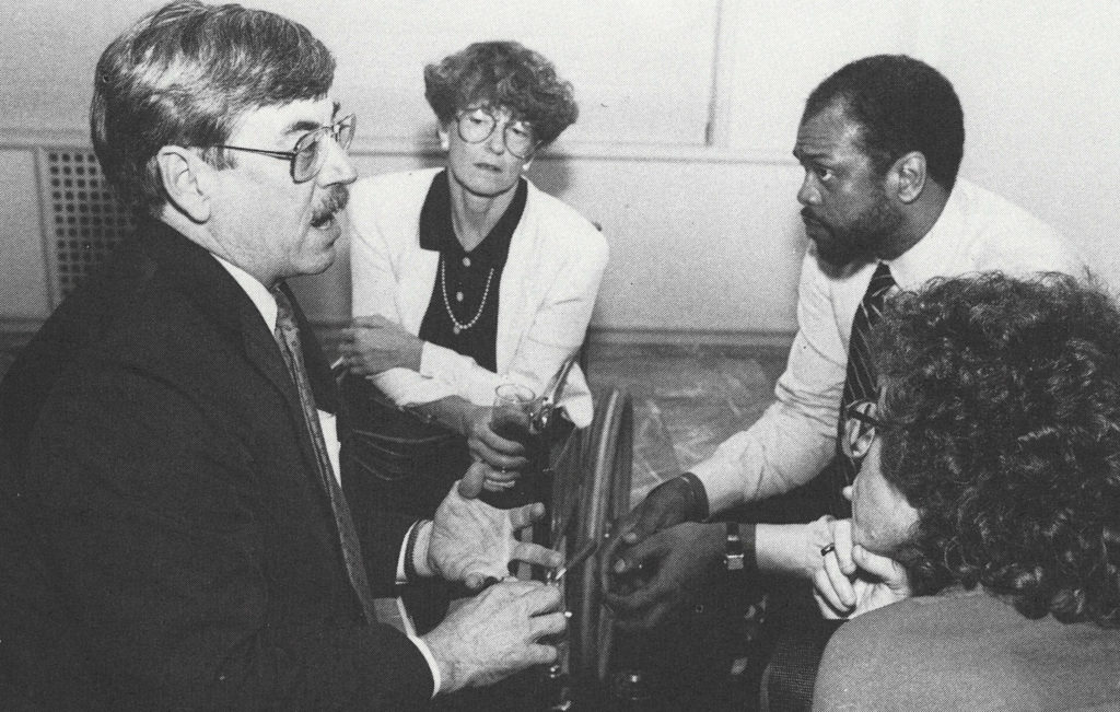 A black and white photo of four professionally dressed people in conversation.