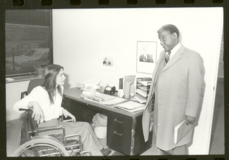 Marca Bristo in her wheelchair at her desk talking to Mayor Harold Washington.