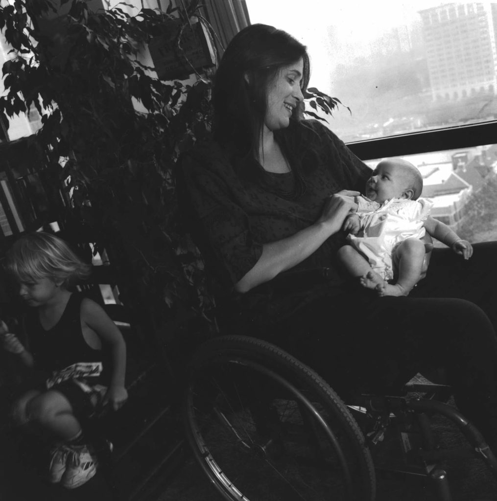 Black and white photo of Marca Bristo sitting in her wheelchair and holding her baby daughter.