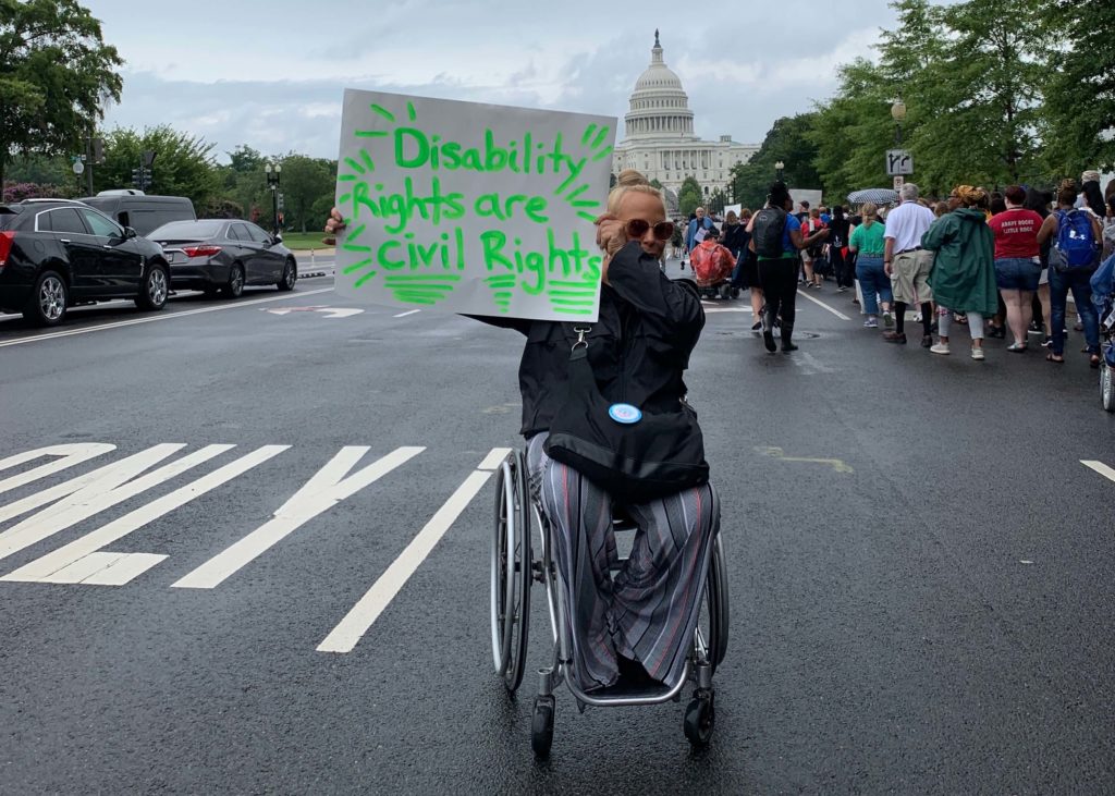 A woman using a manual wheelchair holding a sign that reads "Disability rights are civil rights."