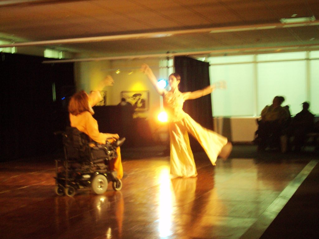 A woman in a wheelchair dances with an abled woman in a integrated dance performance. 