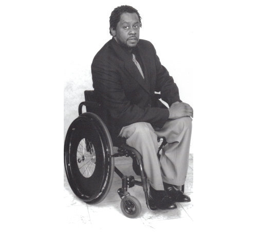 A.E. Hinton, a Black man with glasses, using a wheelchair.
