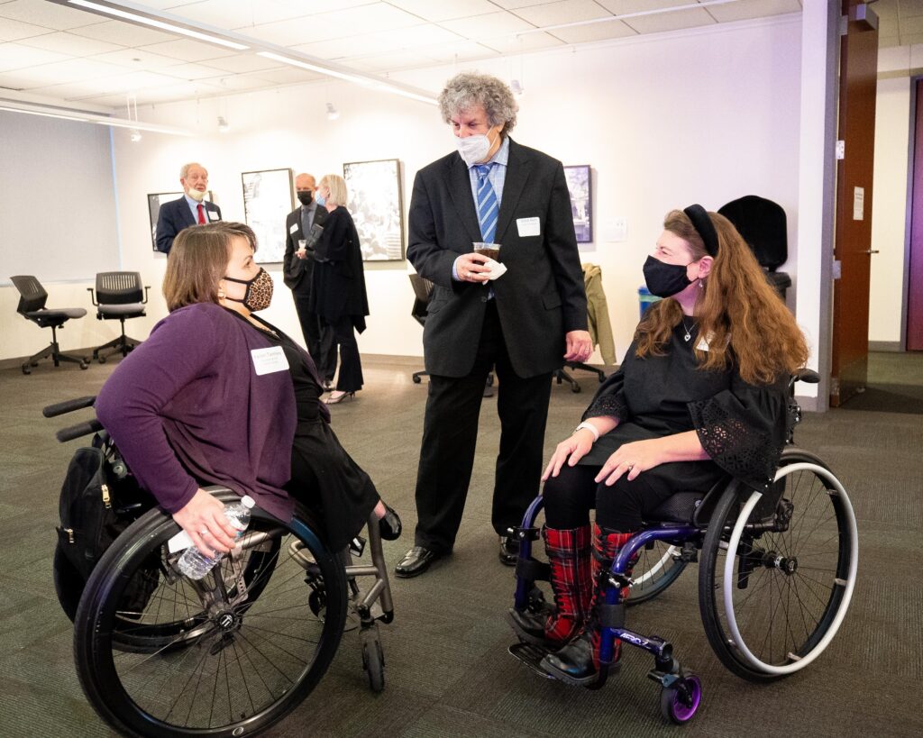 Three people chat together; two are in wheelchairs