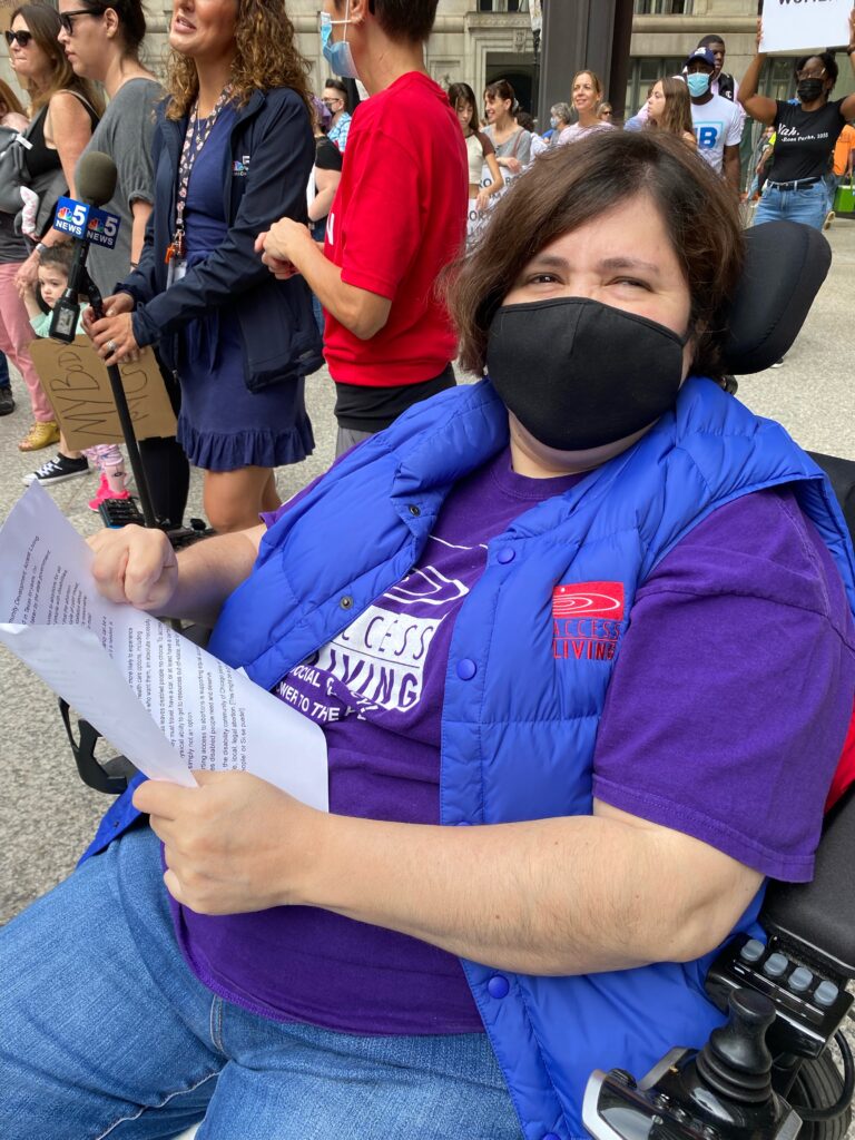 Latina woman in a wheelchair wearing an Access Living shirt and face mask