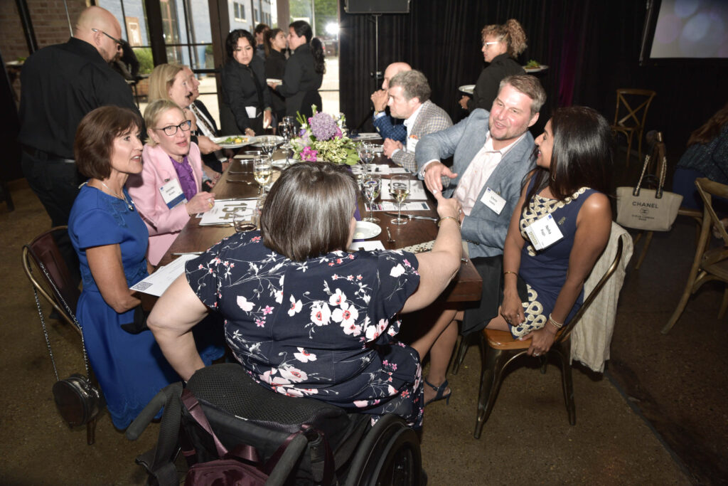 A table of sponsors and their guests during dinner being greeted by CEO Karen Tamley.