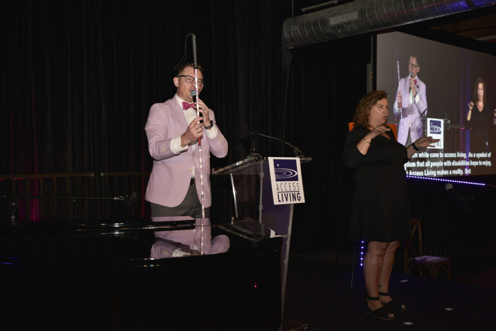 The gala auctioneer holding up an item for auction: a sparkly white cane donated by Lachi to the event.