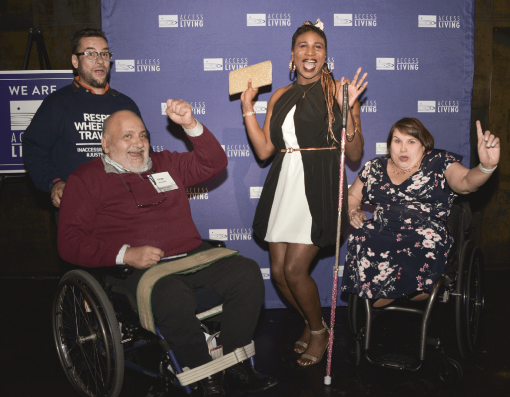 An exuberent group photo of honoree Lachi, CEO Karen Tamley, honored guest Jorge Pineda, and Jorge's personal attendant in front of a purple and white Access Living backdrop.