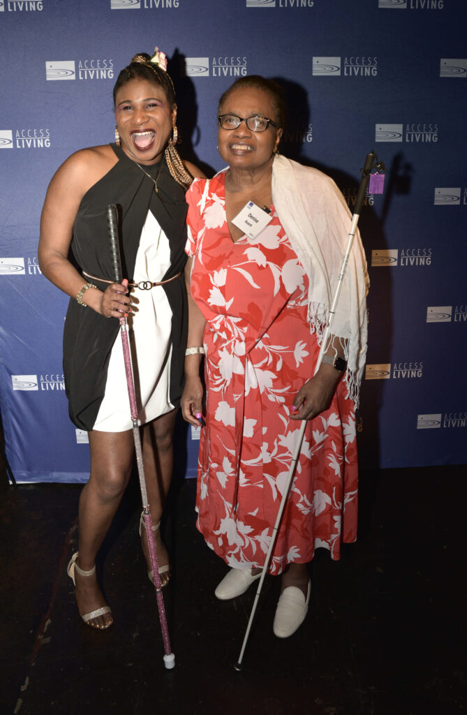 Honoree Lachi with Access Living board member Denise Avant in front of a purple Access Living backdrop. Both are holding white canes. Lachi's is covered in pink rhinestones. Both are smiling happily.