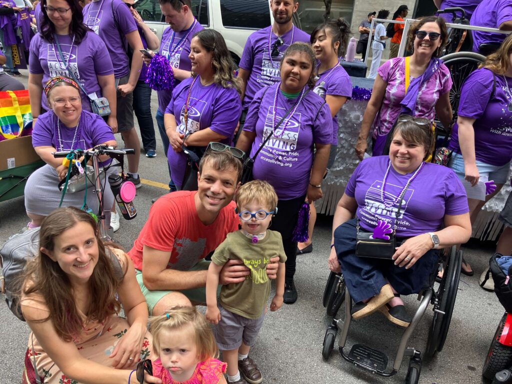 Parade goes in purple Access Living t-shirts with CEO Karen Tamley and two young parents posing with their young children.