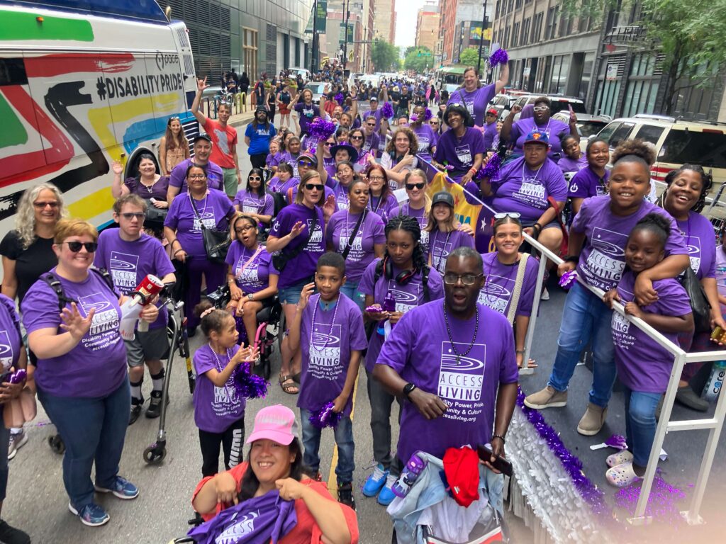A group shot before the parade. The line of parade participants stretches back and out of sight of the camera. Almost everyone is wearing a purple Access Living shirt.