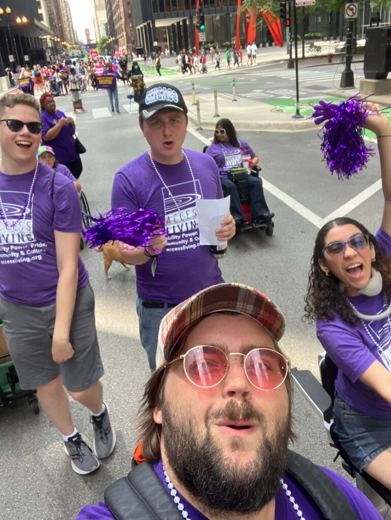 A selfie of four people in Access Living t-shirts as they walk in the parade