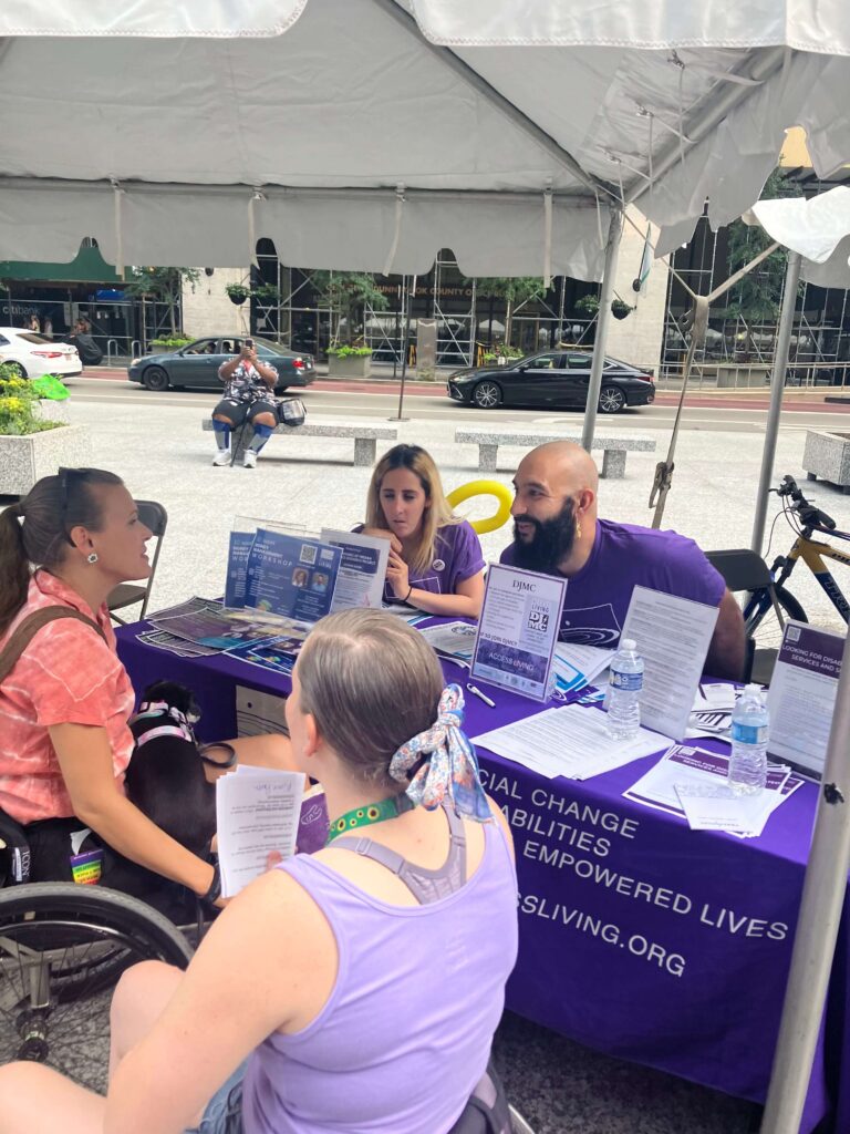 Wheelchair users talk to Access Living staff members sitting behind an informational table
