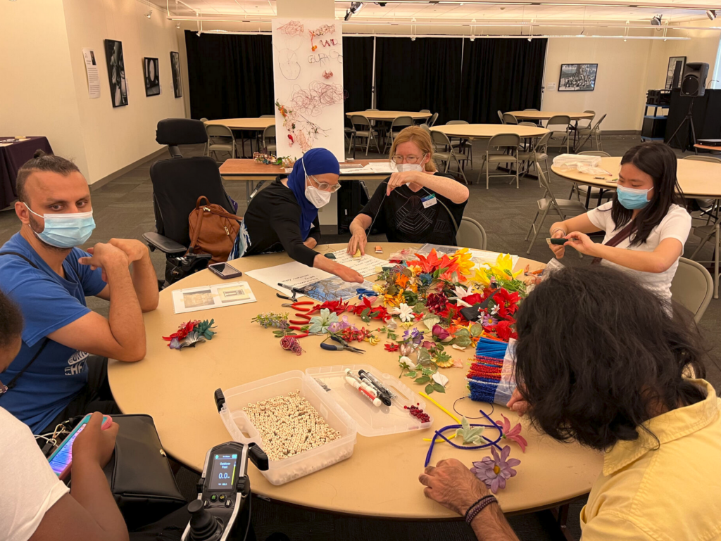 A group of people gather around a table and work on an art project together. 