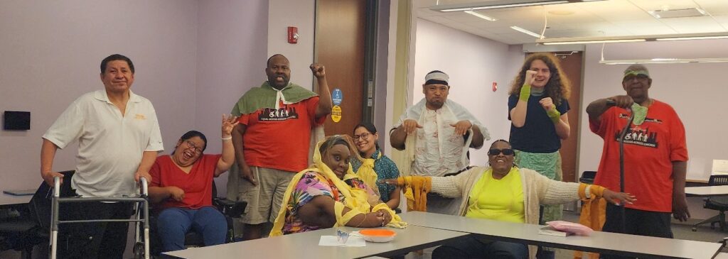 Group of nine Access Living consumers smiling and raising their arms in celebration