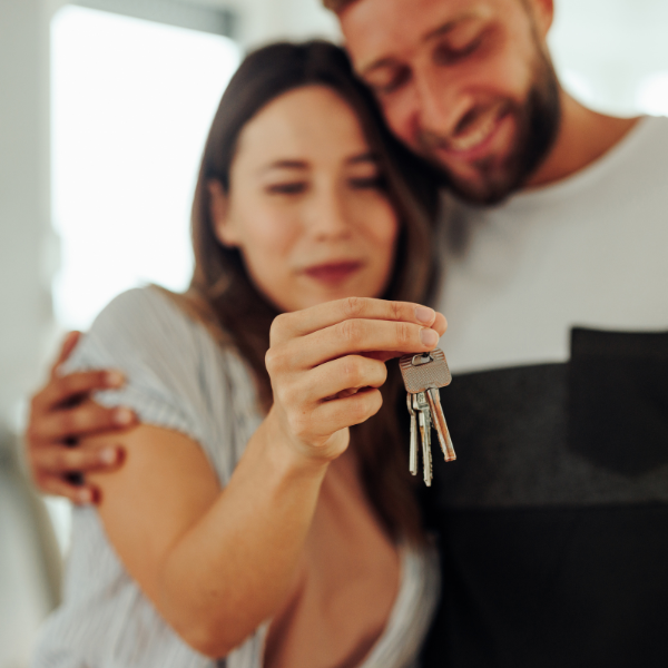 A man and woman hug in the background while the woman holds out a house key